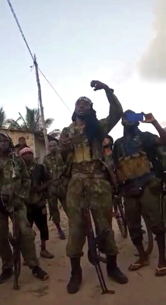 Left: Two insurgents stand in front of a government building in Quissanga with an ISCAP flag. The insurgent in the red bandana calls on others to join their fight and says that the flag of the governing party is not accepted.
   Right: An insurgent addresses the local population in a village in Muidumbe district in early April.
